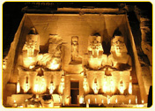 Illuminated facade of the Abu Simbel temple featuring four colossal statues of Ramses II at night.