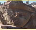 Large stone sculpture fragment depicting a stylized human face with a serene expression.