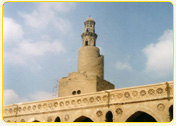 Minaret of a historic mosque with intricate architectural details against a blue sky.