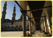 Architectural view of a mosque with minarets and a colonnaded walkway in the foreground.