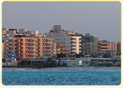 Coastal view of modern buildings along the shoreline with a clear blue sea in the foreground.