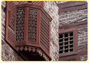 Ornate wooden balcony with intricate latticework on a brick building facade.