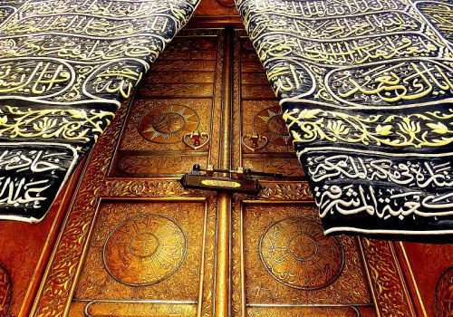 Intricately designed golden doors of the Kaaba adorned with Arabic calligraphy and decorative patterns.