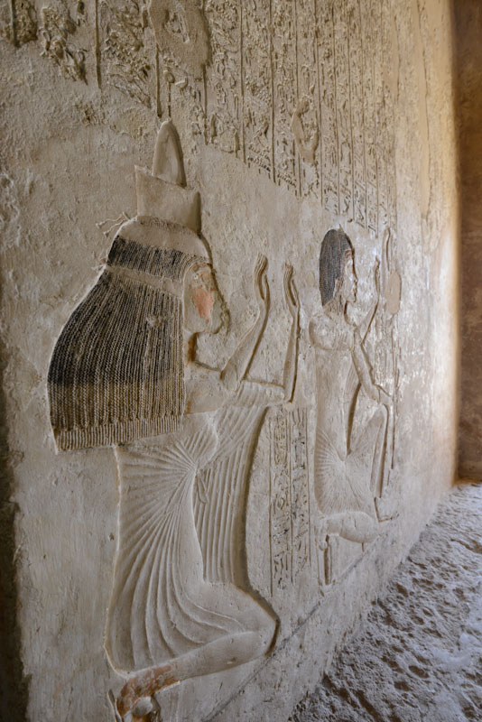 Ancient Egyptian relief depicting two figures with detailed headdresses and clothing on a stone wall.