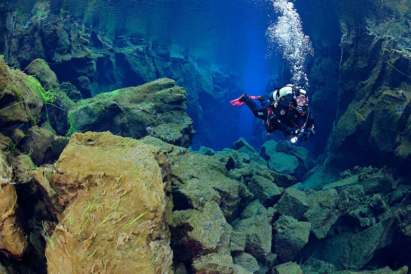 Scuba diver exploring underwater rock formations in a clear blue environment.