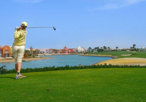 A golfer in a yellow outfit swinging a golf club on a course near a water body.