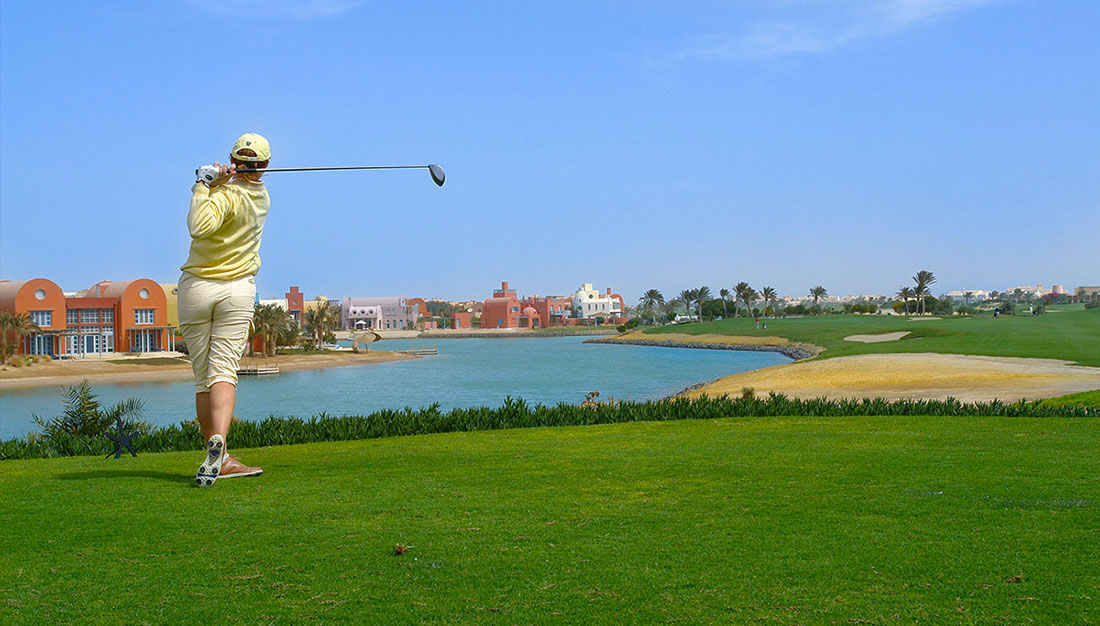 A golfer in a yellow outfit swinging a golf club on a course near a water body.