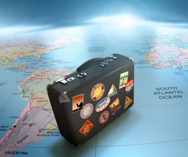 Black suitcase covered in travel stickers placed on a world map highlighting the South Atlantic Ocean.