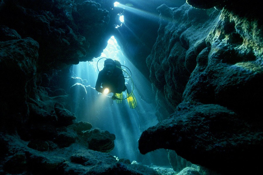 Diver exploring an underwater cave illuminated by beams of sunlight filtering through the water.